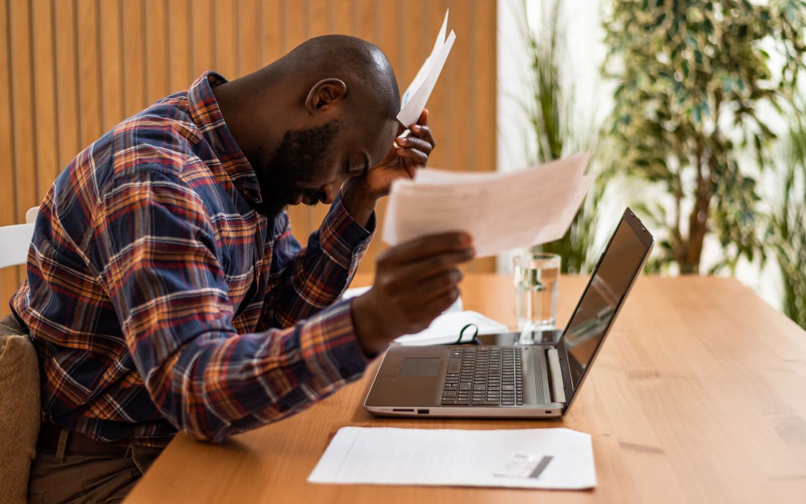 A real estate agent sitting at a desk, head in hand, holding paperwork beside a laptop
